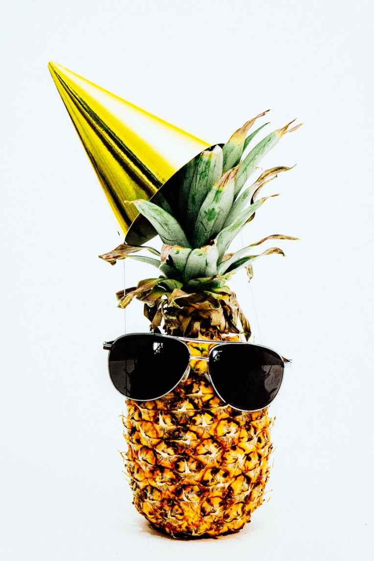 photo of pineapple wearing black aviator style sunglasses and party hat
